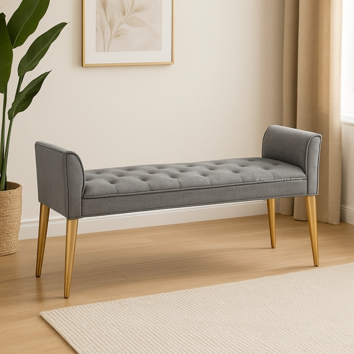 Gray tufted bench with gold legs in a room with a plant and framed picture.